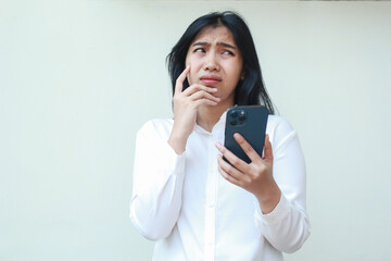 dark hair pondering asian young business woman wear white formal suit using mobile phone app...
