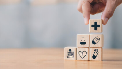 A person is holding up a stack of wooden blocks with a cross on top. The blocks have various medical symbols on them, such as a heart, a stethoscope, and a syringe