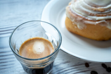 Cinnamon roll on a plate on a wooden background with a glass of espresso next to it