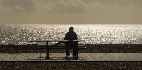 silhouette of a man sitting on a bench looking out to sea
