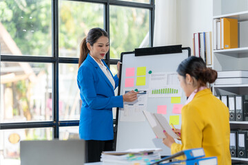 Businesswomen Brainstorming: Two professional women collaborate on a whiteboard filled with colorful sticky notes and charts.