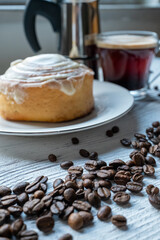 Cinnamon roll on a plate on a wooden background with a glass of espresso next to it