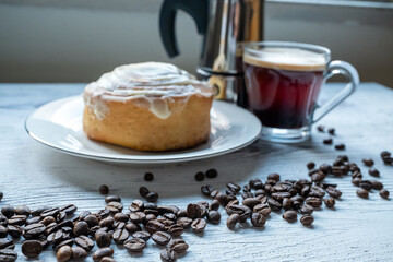 Cinnamon roll on a plate on a wooden background with a glass of espresso next to it