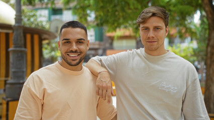 Naklejka premium Handsome adult men smiling and posing in an outdoor urban park, showcasing friendship and a happy relationship in a city setting.