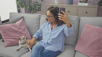 Obraz premium A middle-aged woman takes a selfie with her pet chihuahua on a cozy couch indoors.