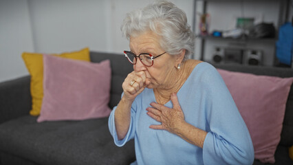 Elderly woman coughing while sitting on a sofa in a living room, expressing discomfort or illness.