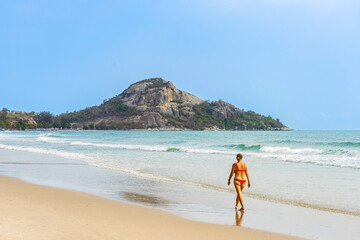 Back view of woman wear red bikini walk on beach. Happy mature woman while walking along the beach. Carefree lady walking on coastline at beach. Concept of senior lifestyle,travel,relaxing in nature.