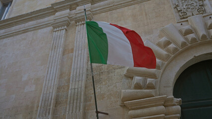 An italian flag waves proudly against the stone facade of a historic building in lecce, puglia,...