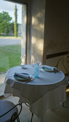 A cozy indoor italian restaurant setting with a neatly set table for two near a window overlooking a scenic outdoor view.