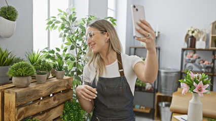 A smiling young woman takes a selfie in a florist shop surrounded by green plants and flowers.