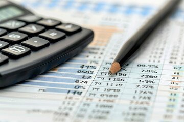 A calculator rests next to a sharpened pencil, both positioned over detailed spreadsheets filled with financial data and analysis figures for an ongoing business review