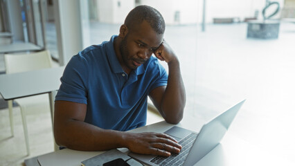 Young african american man working in office room on laptop while looking focused indoor