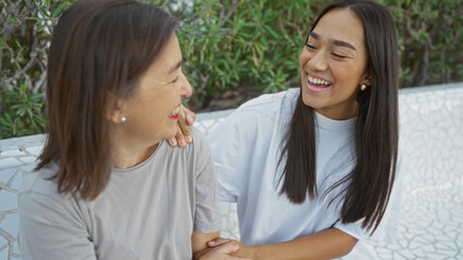 Woman smiling at her mother while sitting outdoors, showcasing family love and connection in an urban park setting, depicting a warm and joyful interaction between two women in a city environment.