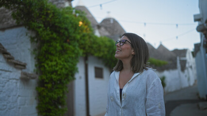 Young hispanic woman exploring the charming streets of alberobello, italy, surrounded by historic trulli houses.