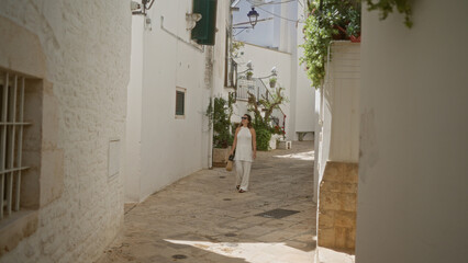 Obraz premium Young hispanic woman walking through the charming white streets of the old town in locorotondo, puglia, italy, surrounded by traditional architecture.