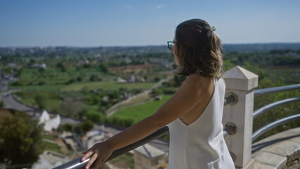 Young hispanic woman enjoying stunning viewpoint in locorotondo, puglia, italy, overlooking scenic countryside and old town streets.