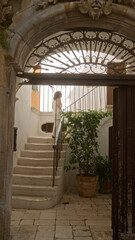 Young hispanic woman walking up stairs in the charming old town streets of locorotondo, puglia, italy, under an ornate stone archway.