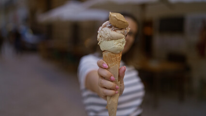 A beautiful young woman in lecce, puglia, holds an ice cream cone with multiple scoops in the foreground, showcasing a charming italian street scene.