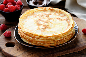 Freshly baked stack of homemade crepes or thin pancakes with fresh berry and chocolate sauce in rustic style.