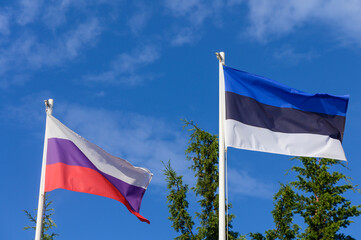 Flags of Russia and Estonia waving under a clear blue sky in a serene, peaceful setting surrounded by lush greenery