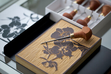 Detailed View of a Linocut Block with a Floral Design, Accompanied by a Carving Tool
