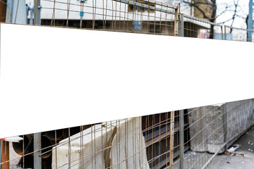 Blank white banner attached to rusty wire fence at construction site with industrial materials and equipment in background © Bonsales