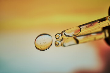 A pipette with facial serum against a sunset background in bright orange tones.