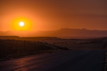 HDR Sunset layers of mountains in the background orange clouds beautiful rolling hills farm in Wyoming and bright sun on country road