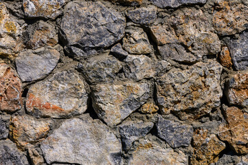 Textured stone wall composed of various sized rocks, showcasing natural colors and patterns under bright daylight