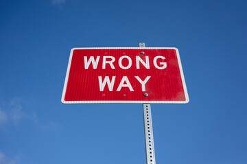 Low angle view of a Wrong Way sign against the blue sky background.