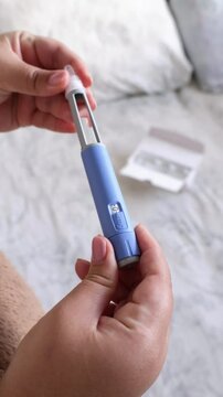 A vertical close up of a young woman priming the pen injector, prepering it for injection