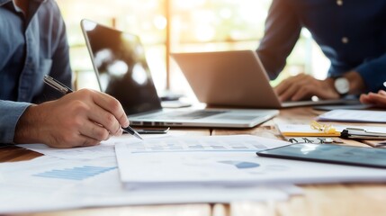 A collaborative workspace featuring hands engaged in note-taking, with laptops and documents on a table, symbolizing teamwork and productivity.