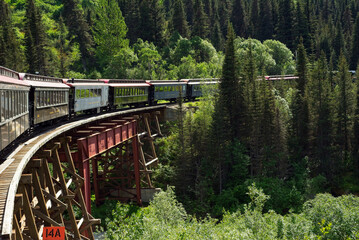A passenger excursion train rounds a curved bridge over a ravine near Skagway, Alaska.