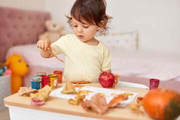 happy little child girl painting autumn leaves. baby girl drawing leaves in yellow and orange paint