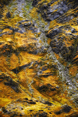 The landscape showcases a blend of golden and orange autumn foliage, contrasting against rugged rocky terrain, evoking the beauty of nature in a mountainous region.