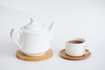 A simple white teapot and a white mug with tea on a gray background