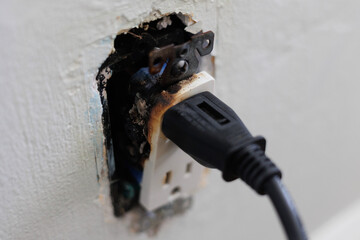A close-up of a burnt electrical outlet with a plug still inserted, showing signs of damage from an...