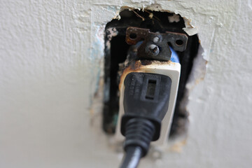 A close-up of a burnt electrical outlet with a plug still inserted, showing signs of damage from an...