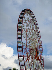 Ferris wheel from bottom to top. Attraction cabins against the gray sky.  Red and white Ferris wheel