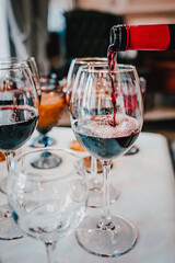 A person pours red wine into a stemmed glass, with other glasses in the background. The scene is elegant and inviting, perfect for wine tasting or a sophisticated gathering