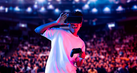 Adult holding joystick and wearing VR goggles while enjoy playing games at stadium with blurring background. African man enjoy controlling controller and using augmented reality technology. Ingenuity.