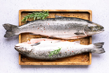 Big raw salmon with herbs and spices on the wooden tray on light marble background top view.
