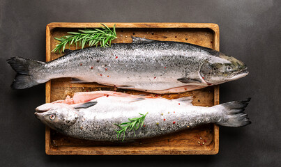 Big raw salmon with herbs and spices on the wooden tray on black stone background top view.
