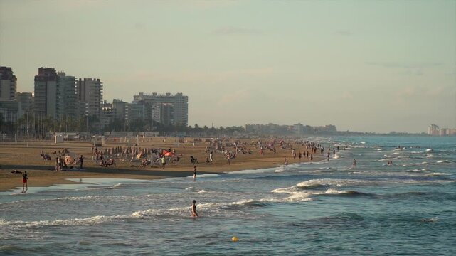 Slow motion, panoramic view of a beach with people at sanset.
