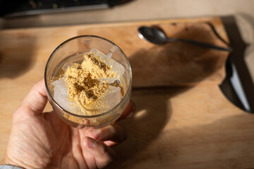 A glass filled with ice cubes and powdered Amanita muscaria mushroom on its surface, held in the hand, illuminated by natural sunlight. Preparing a homemade fly agaric elixir