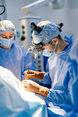 Surgeons in a modern operating room. Two surgeons dressed in scrubs collaborate closely to perform...