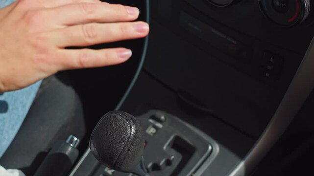 A close-up of a woman's hand switching gears in an automatic transmission. The woman puts the handle of the automatic transmission in the driving position and drives off. High quality 4k footage