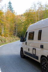 Side of a moving camper van traveling along a picturesque road through a beech forest. Concept: Camper life, tourist destinations, freedom traveling, discovering the world,