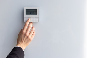 Close-up of hand adjusting digital thermostat set to 25 degrees Celsius. Concept of energy efficiency, climate control, and modern technology in home or office environment.