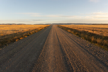 Naklejka premium Rural country dirt gravel road, western ranch lane at sunrise, rural street at sunset, centered